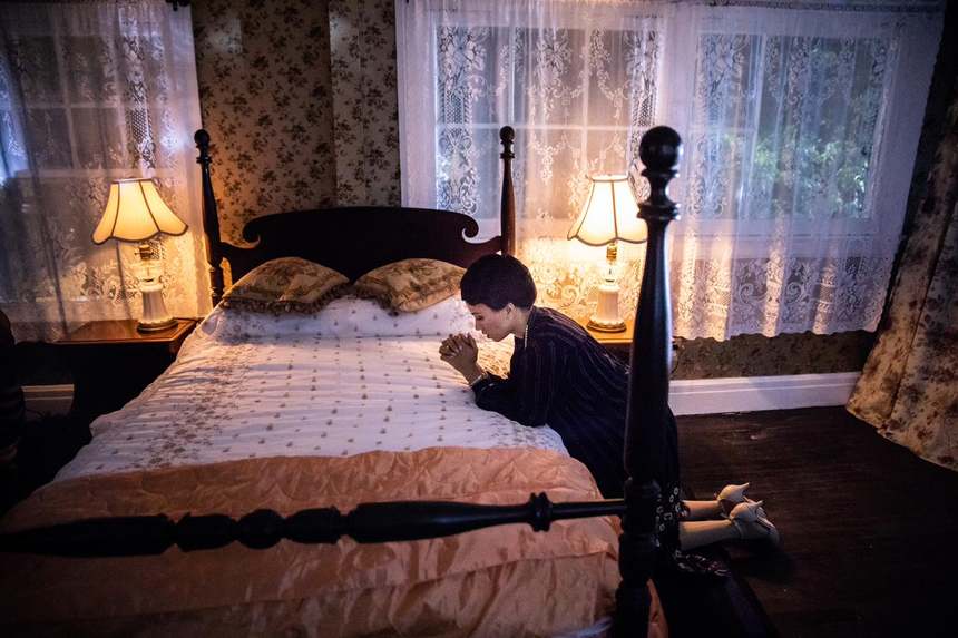 Film frame: Gladys kneeling at the bed in lamplight.